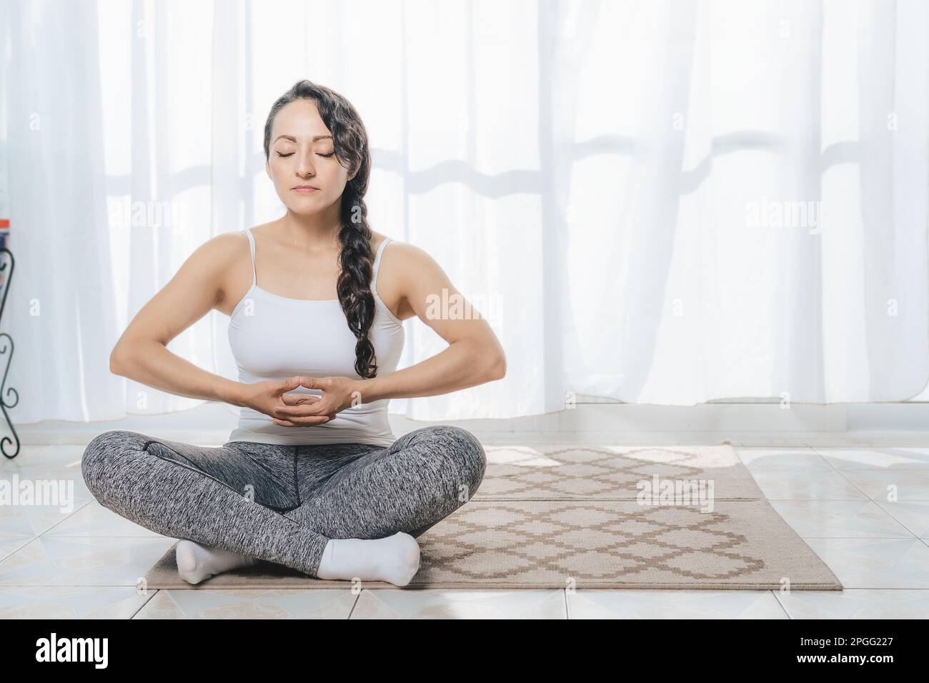 A woman does Yoga indoors, lots of sunlight comes in through the window, she does deep meditation postures. It is very quiet. Stock Photo