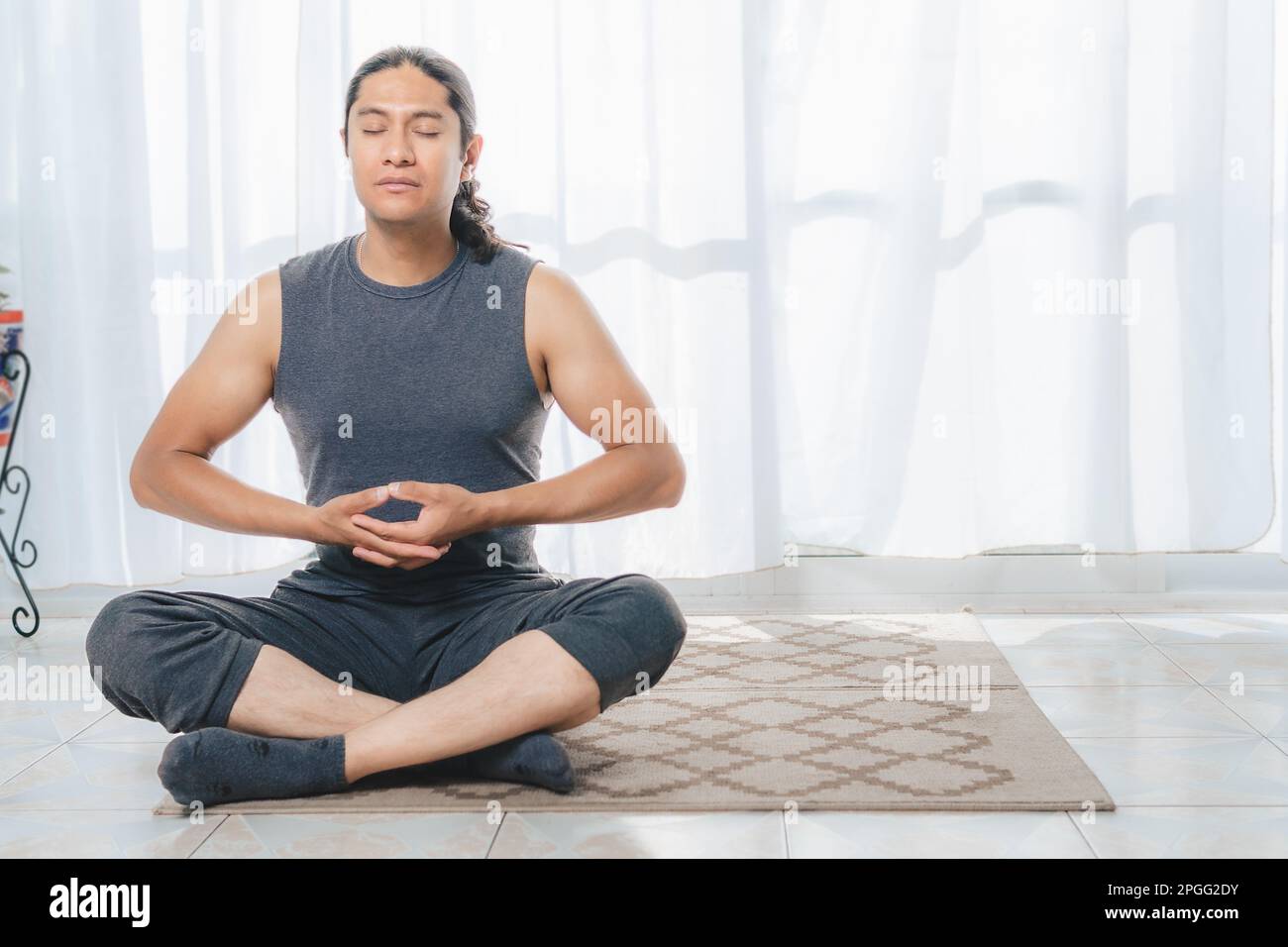 A man does Yoga indoors, a lot of sunlight comes in through the window, he does deep meditation postures. It is very quiet. Stock Photo