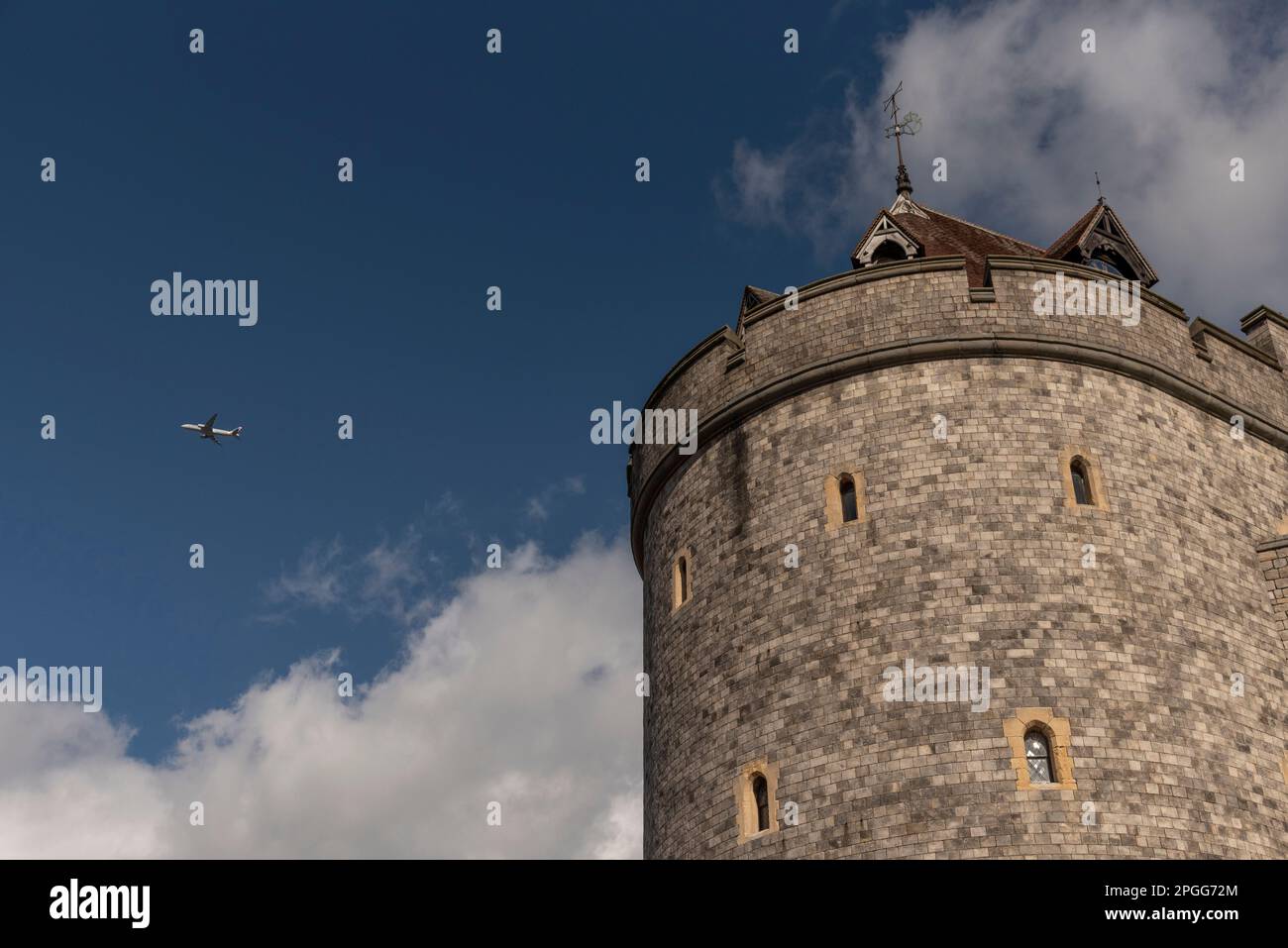 Windsor, Berkshire, England, UK. 2023.  The Curfew Tower of Windsor Castle and a passenger jet flying closeby. Stock Photo