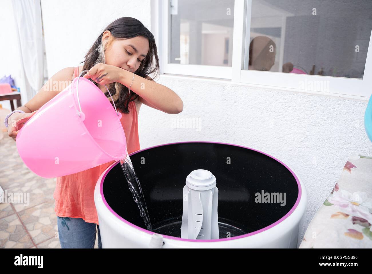 A young woman is manually pouring water into an old top load washing