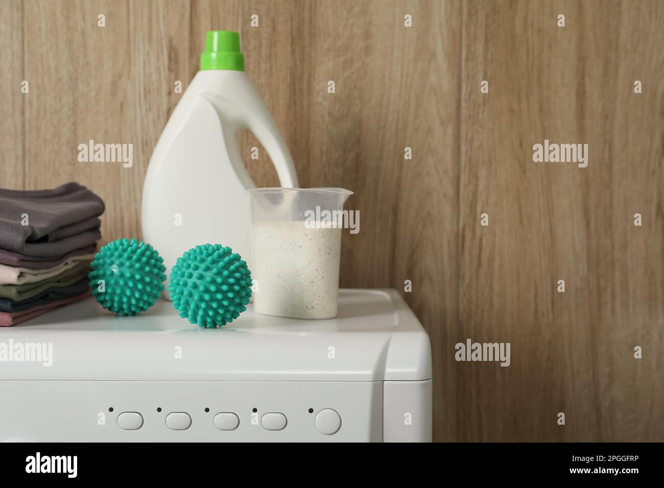 Dryer balls, stacked clean clothes and detergents on washing machine. Space for text Stock Photo