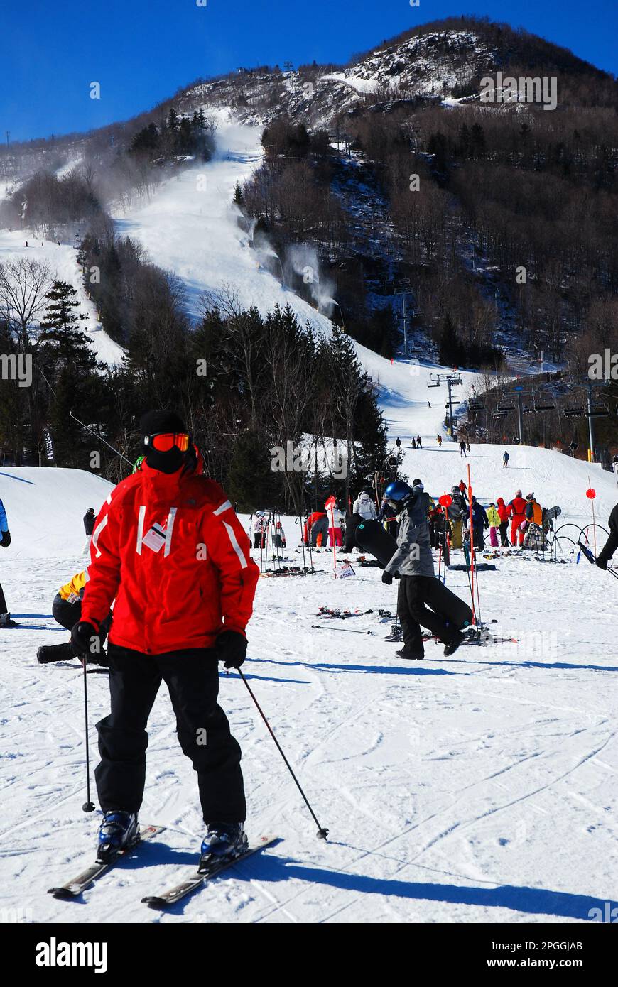 A rescue worker at a ski resort, wearing a red jacket, ensures the skiers are safe on the mountain slopes in winter Stock Photo