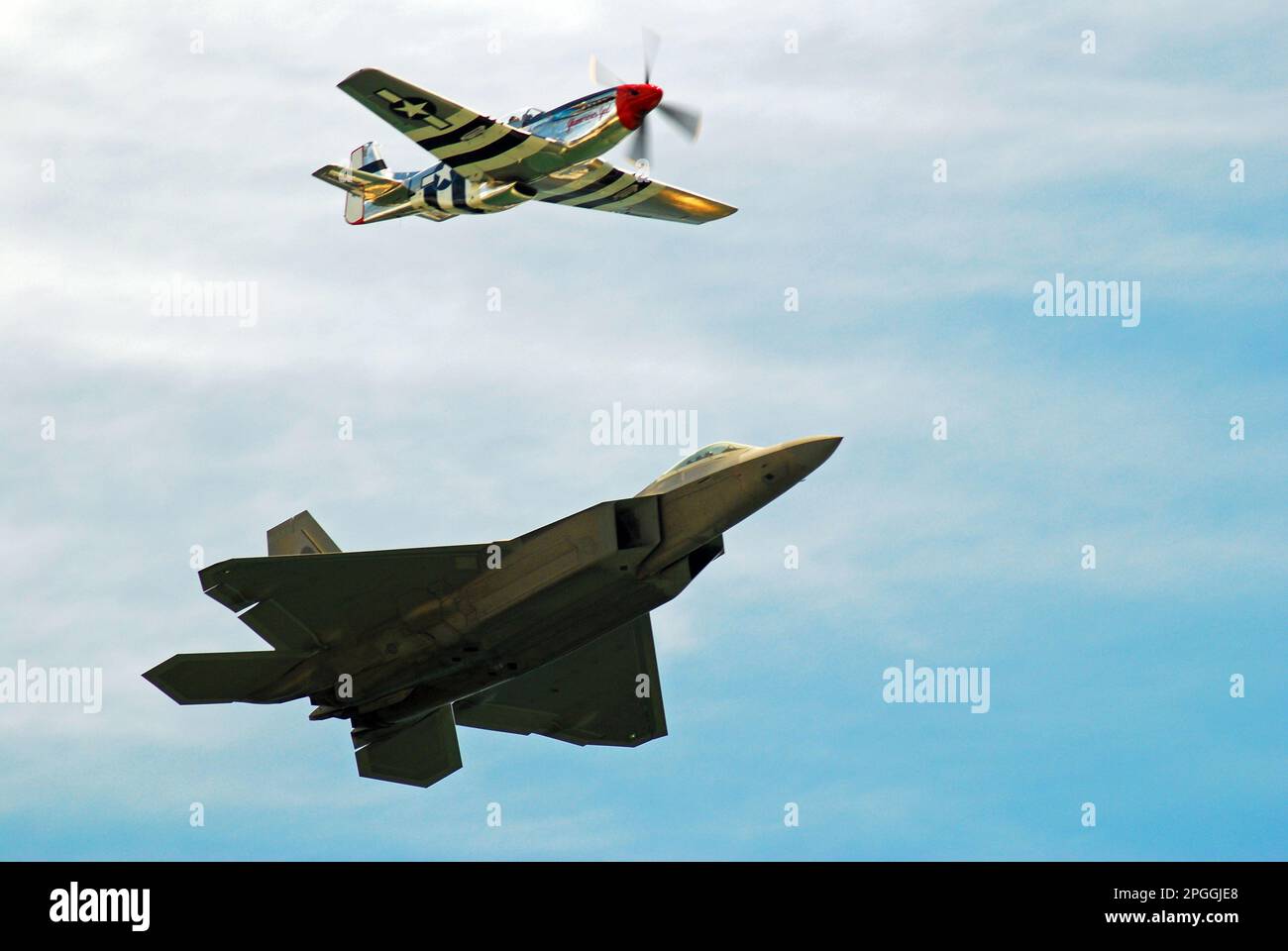 A modern F22 Raptor jet and a World War II P51 Mustang airplane fly side by side in the sky, representing two eras of flight and military aviation Stock Photo