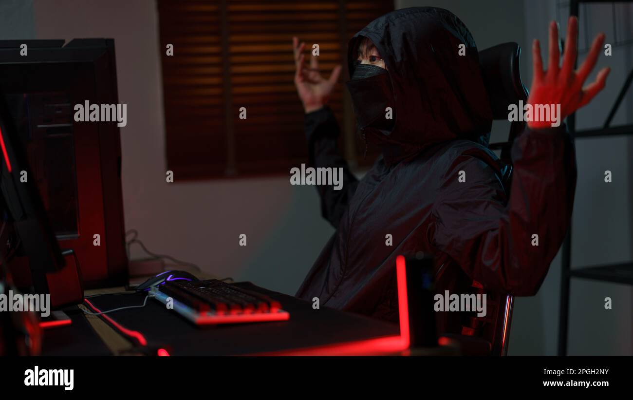 Hacker in hoodie raising hands while having problem with hacking programming system or server. Stock Photo