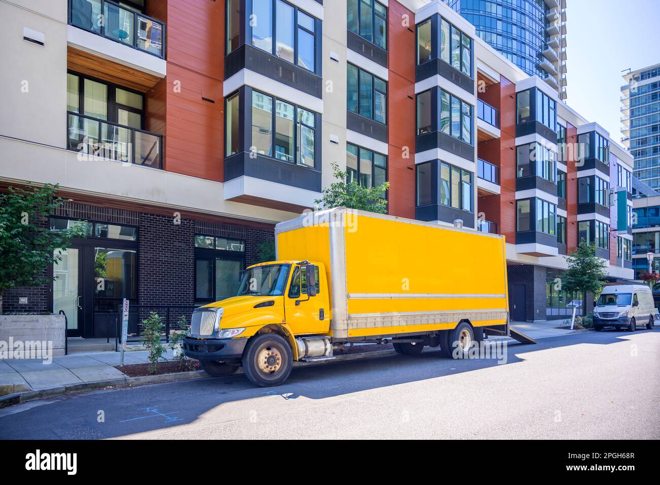 Industrial yellow middle rig day cab semi truck tractor with long box trailer make a delivery to customers to urban city apartment residential multi s Stock Photo