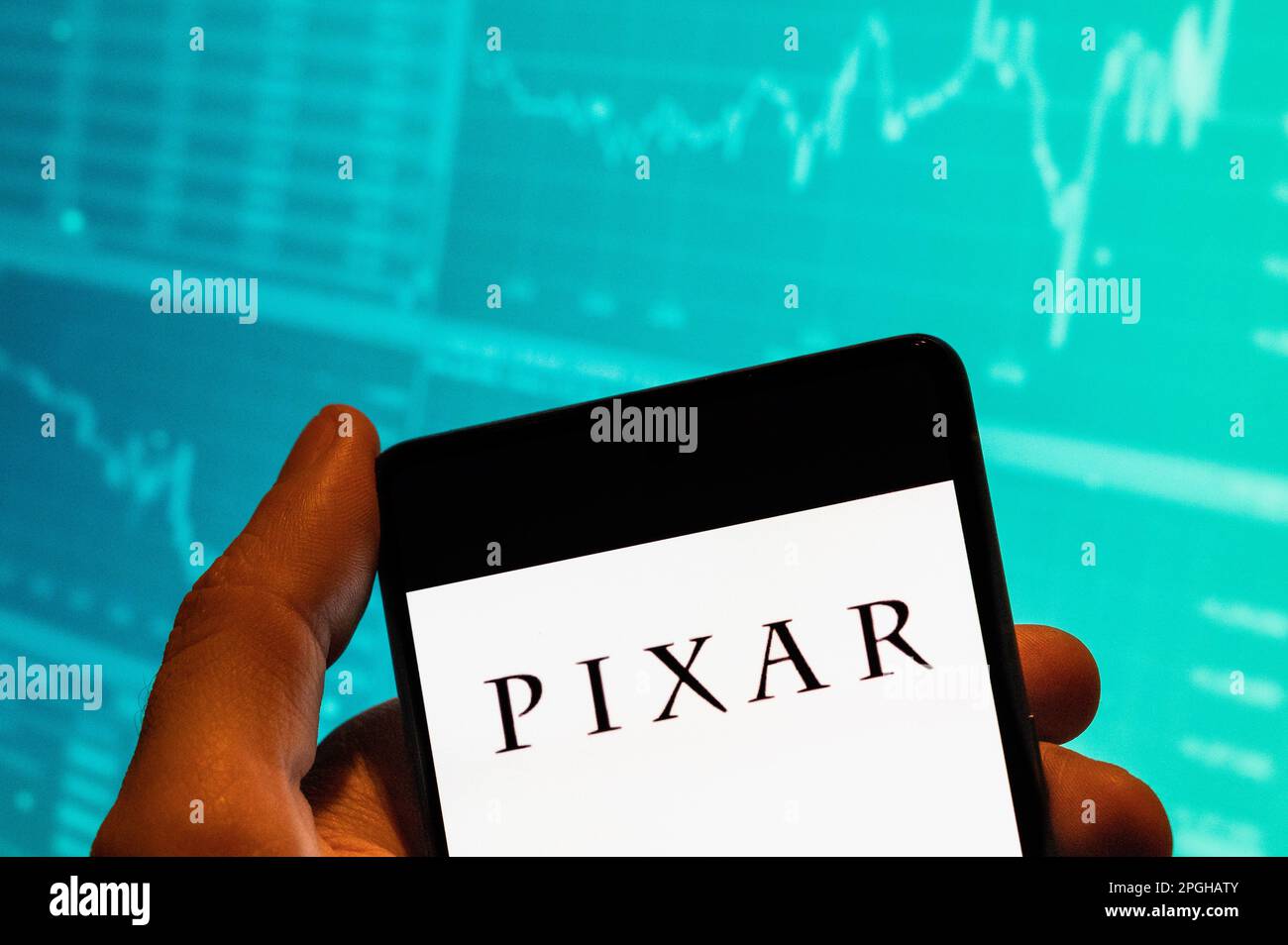 In this photo illustration, the American computer animation film studio  owned by Disney, Pixar logo seen displayed on a smartphone with an economic  stock exchange index graph in the background Stock Photo -
