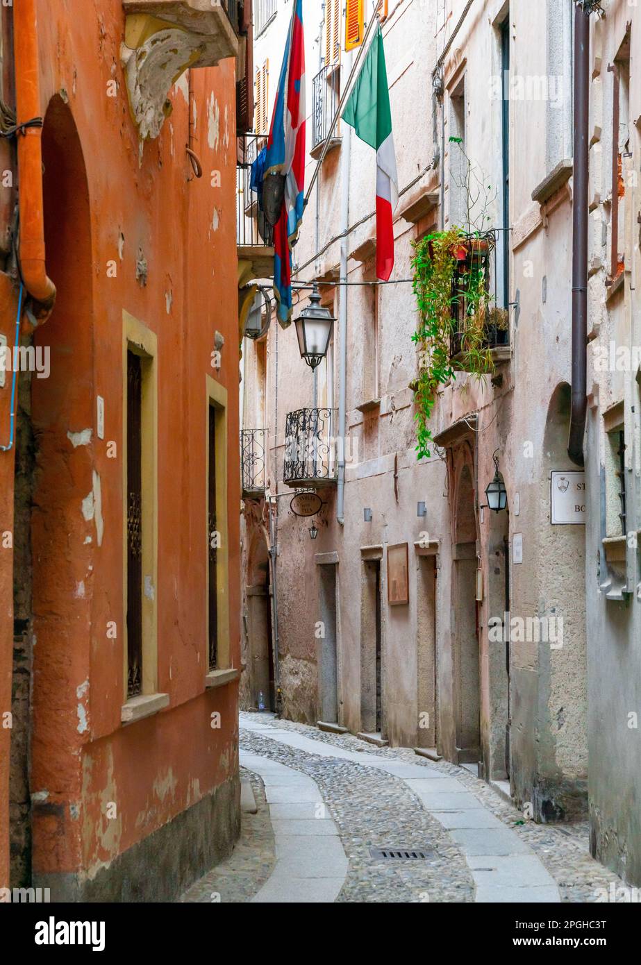 Orta San Giulio, Italy - 13 March, 2023: narrow cobblestone street with shabby buildings and Italian flag Stock Photo