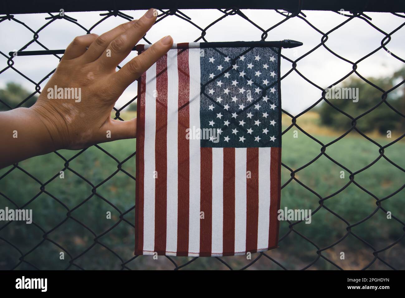 Close up of a American Flag in hand attached to a chain link fence. American immigration and United States refugee crisis concept Stock Photo