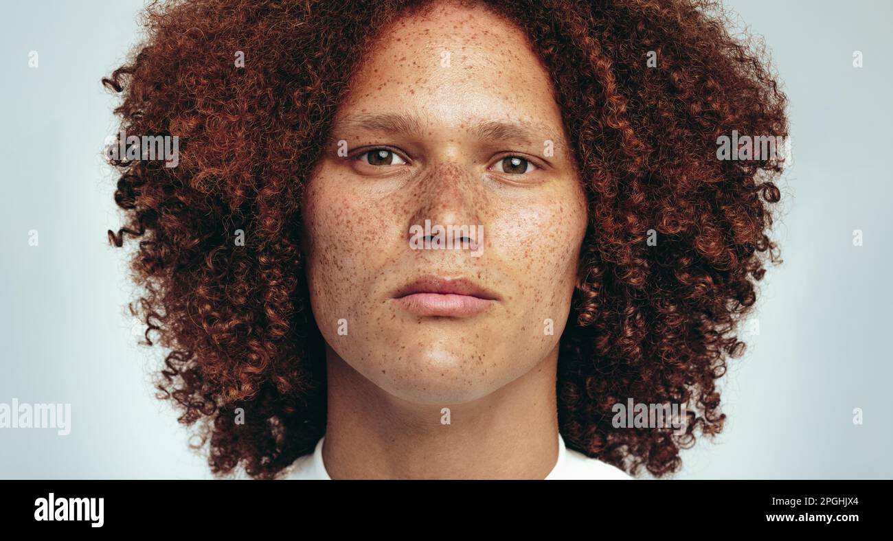 Portrait of a handsome young man with freckles and a curly afro looking at the camera in a studio, expressing confidence in his unique appearance. You Stock Photo