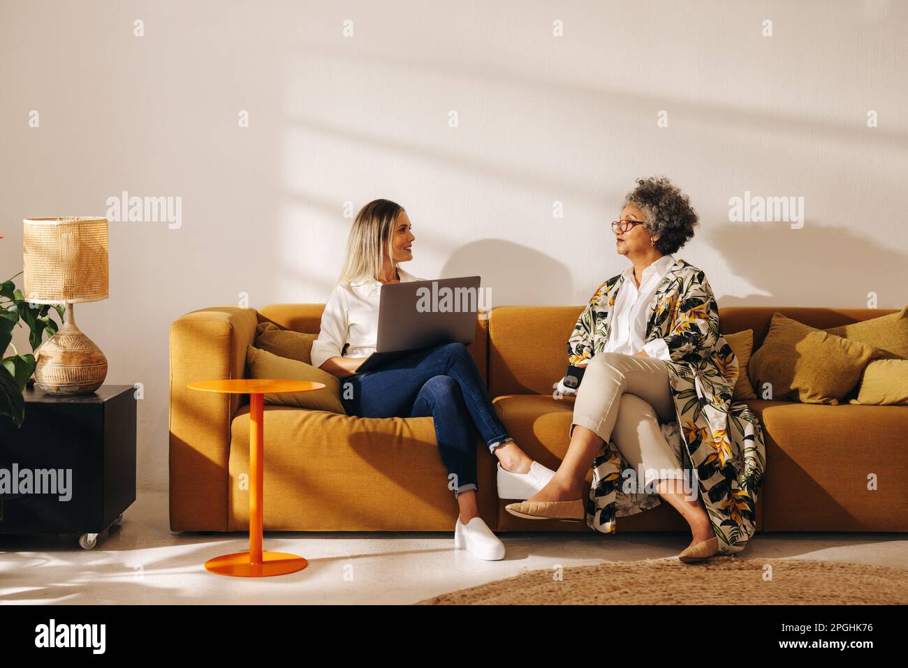 Female entrepreneurs having a discussion while working together in an office lobby. Two diverse businesswomen sitting on a couch in a woman-owned comp Stock Photo
