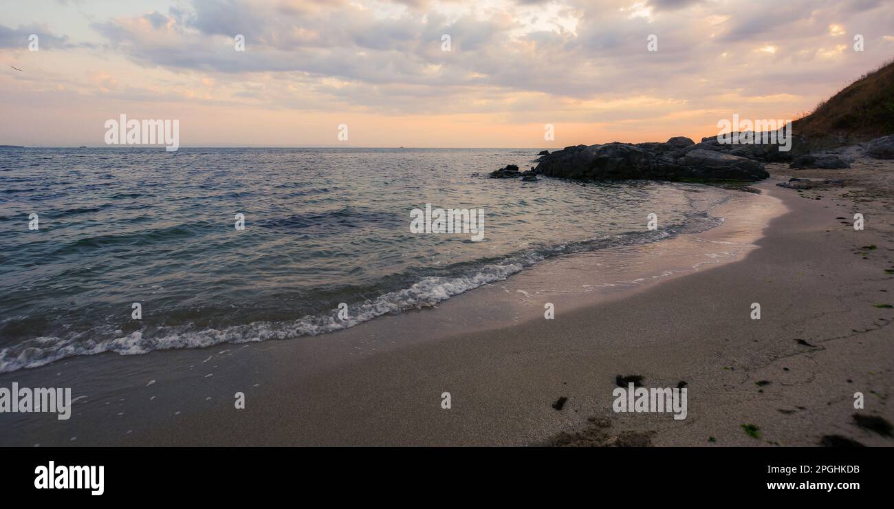 beach of the black sea in bulgaria at dawn. wave washing the sandy coast with rocks beneath a cloudy sky. leisure season in summer Stock Photo