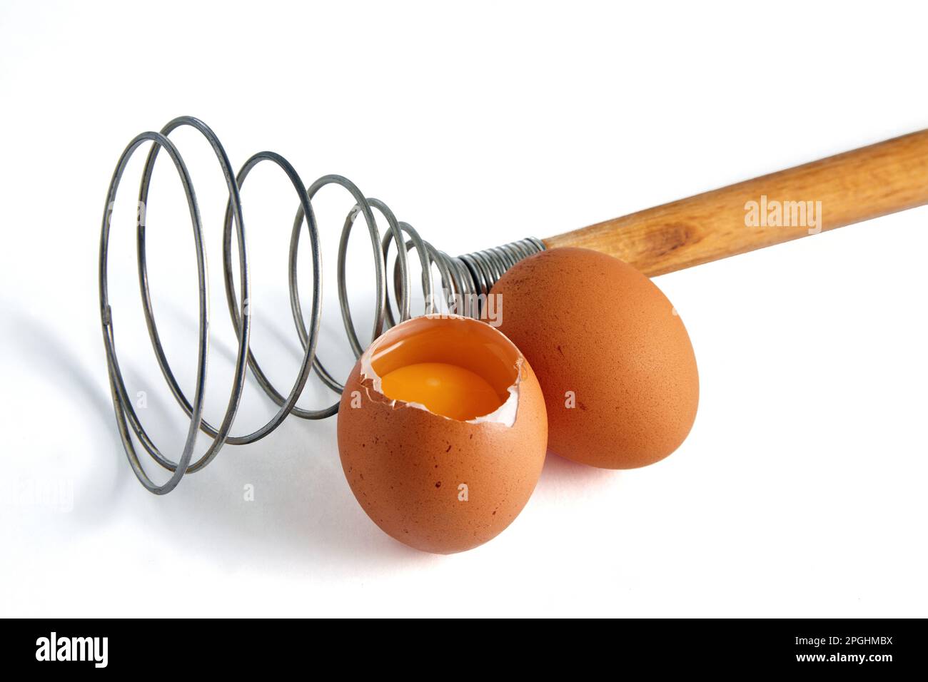 Two beige chicken eggs and a rare eggbeater for beating. Ingredients for cooking isolated on