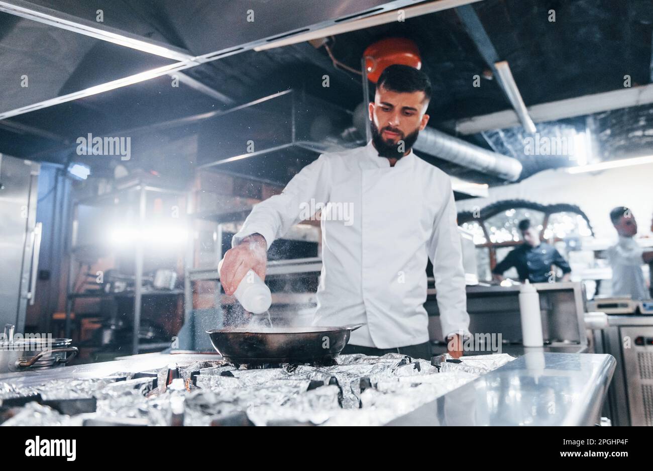 Uses frying pan. Chef in white uniform cooking food at kitchen. Busy ...