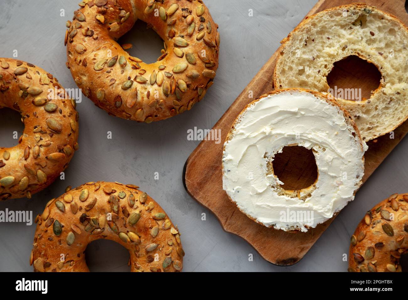 Homemade Whole Grain Bagel with Cream Cheese on a rustic wooden board, top view. Stock Photo