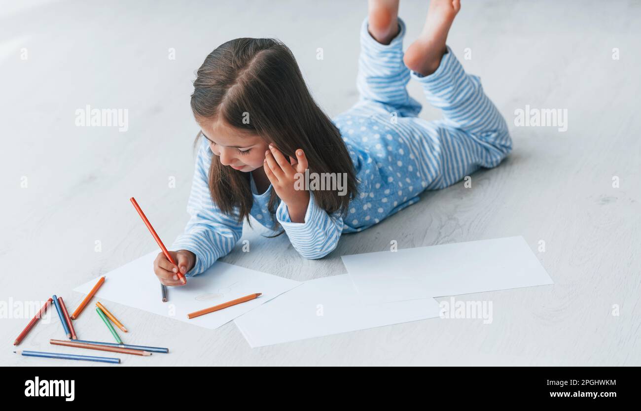 Lying on the floor and drawing. Cute little girl indoors at home alone ...