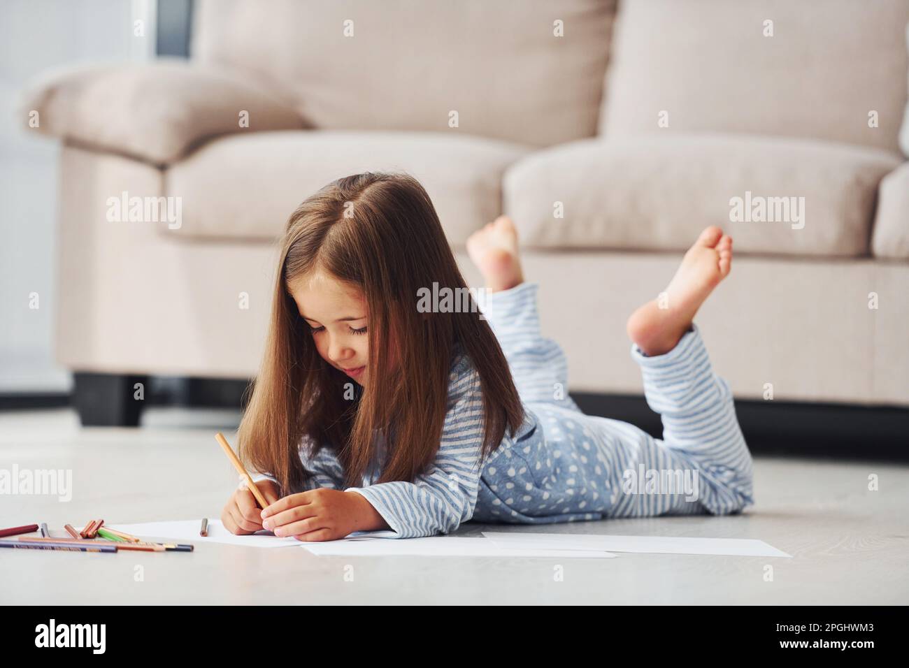 Lying on the floor and drawing. Cute little girl indoors at home alone ...