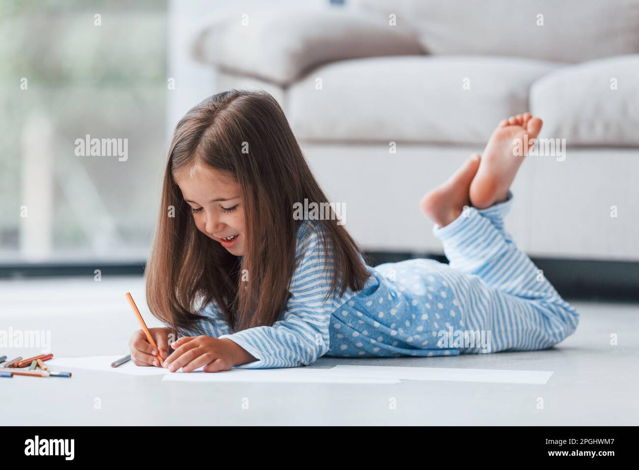 Lying on the floor and drawing. Cute little girl indoors at home alone ...