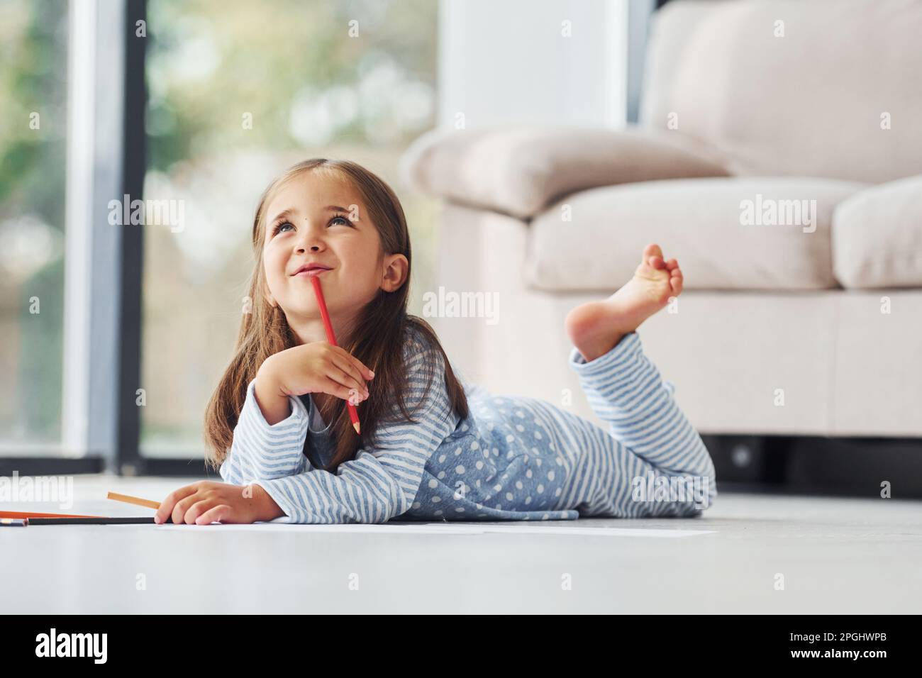 Lying on the floor and drawing. Cute little girl indoors at home alone ...