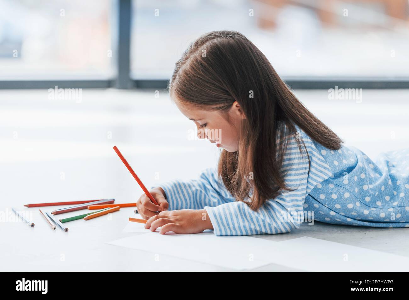 Lying on the floor and drawing. Cute little girl indoors at home alone ...