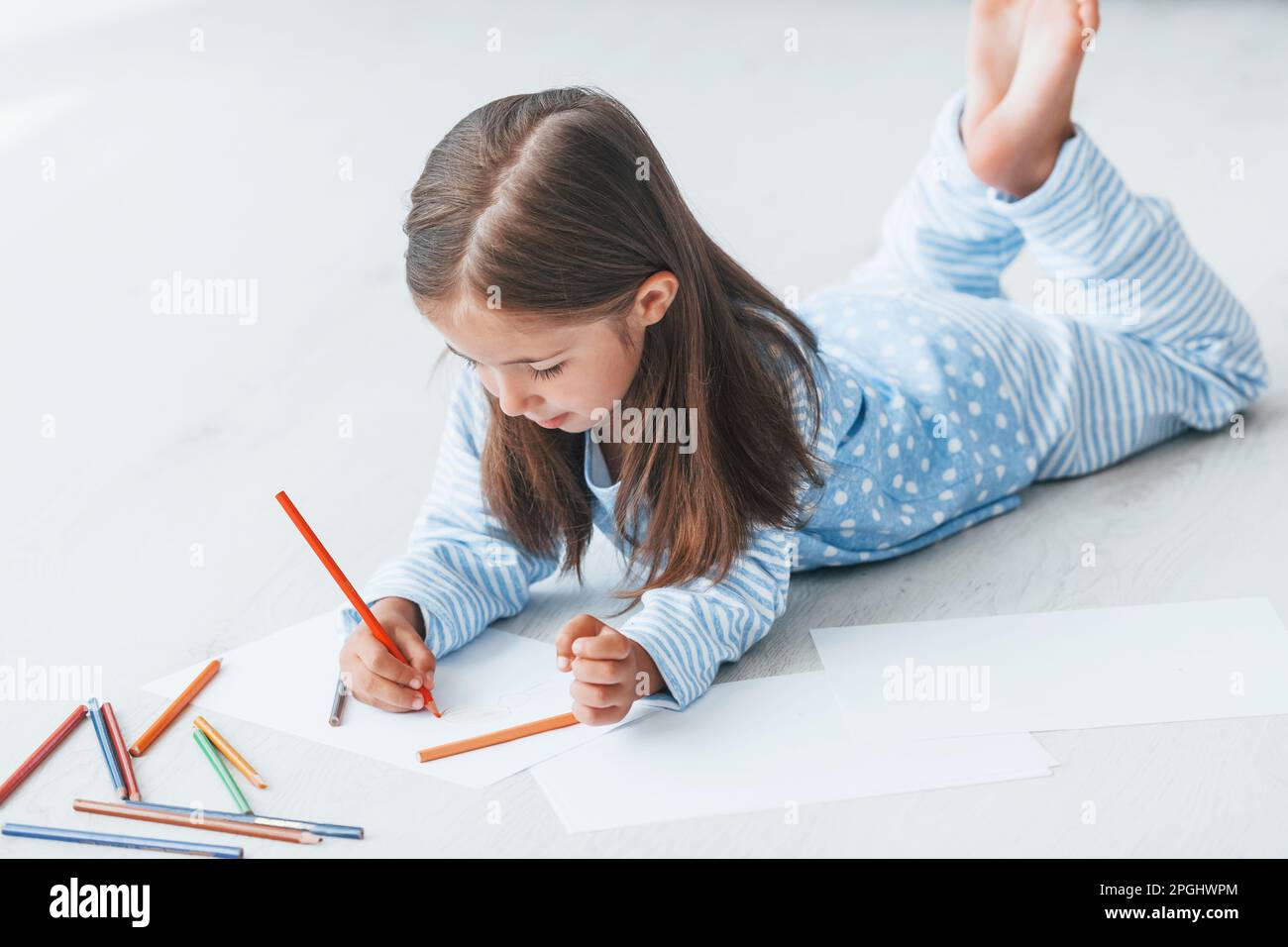 Lying on the floor and drawing. Cute little girl indoors at home alone ...