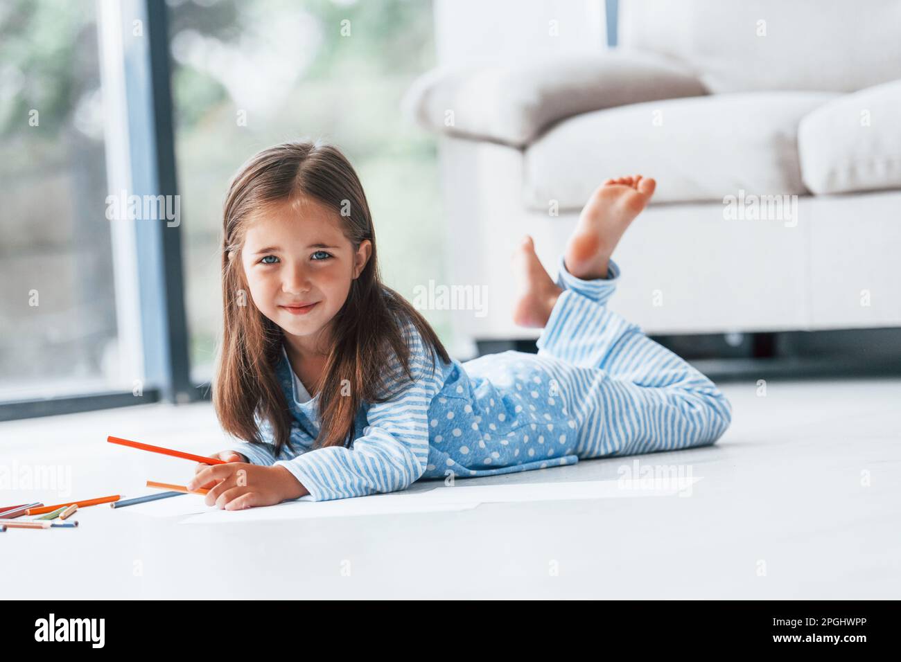Lying on the floor and drawing. Cute little girl indoors at home alone ...