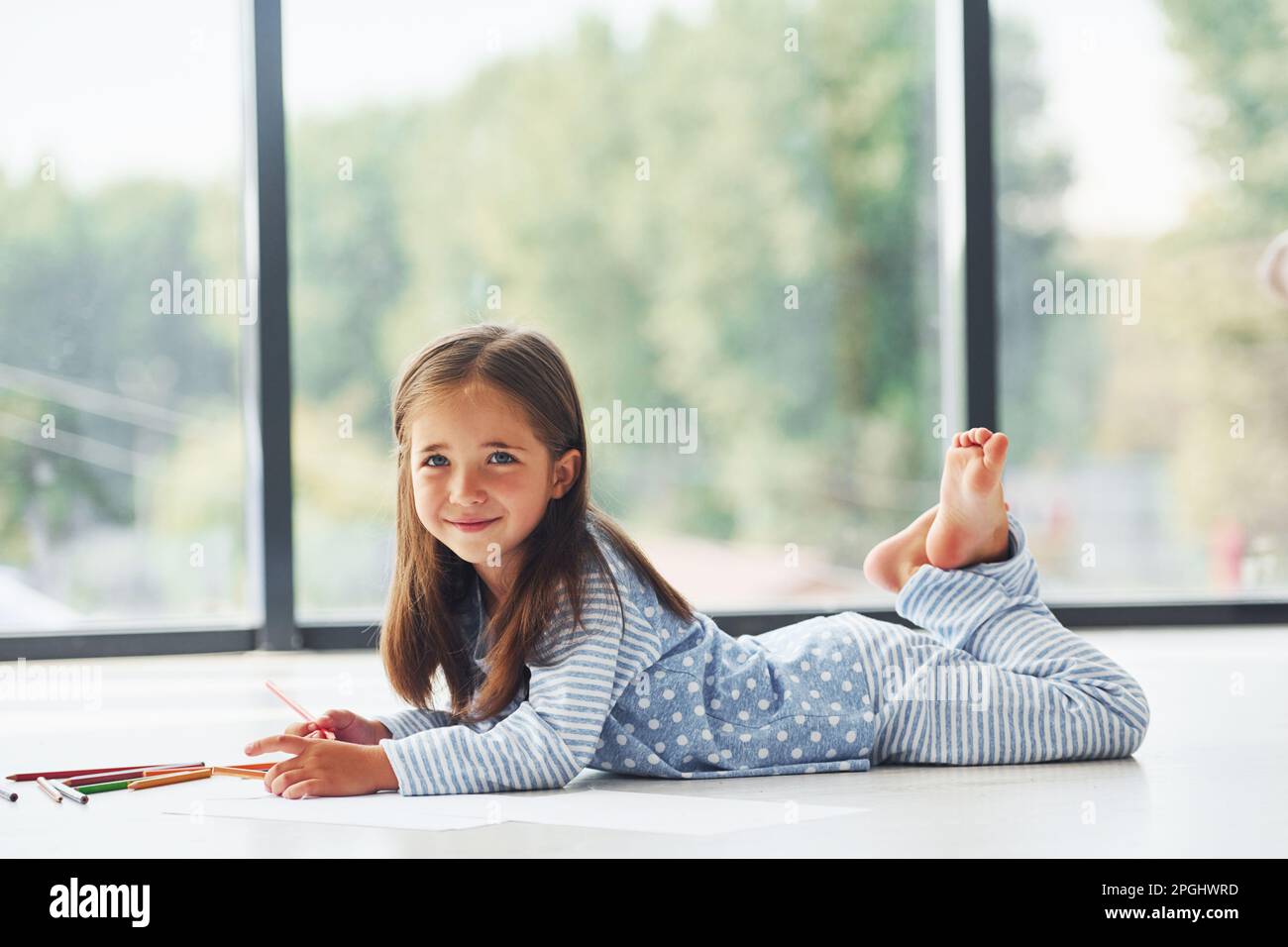 Lying on the floor and drawing. Cute little girl indoors at home alone ...