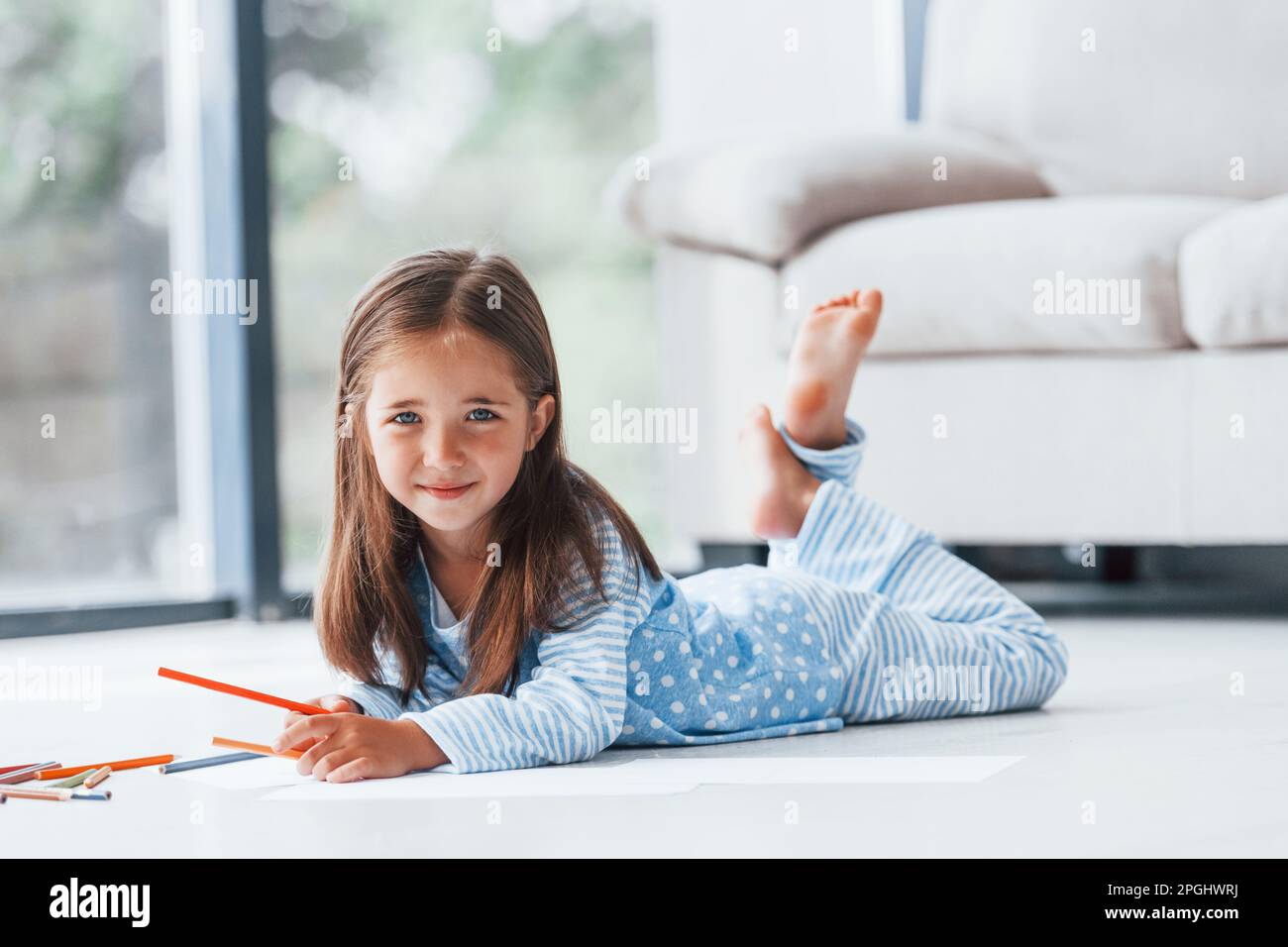 Lying on the floor and drawing. Cute little girl indoors at home alone ...
