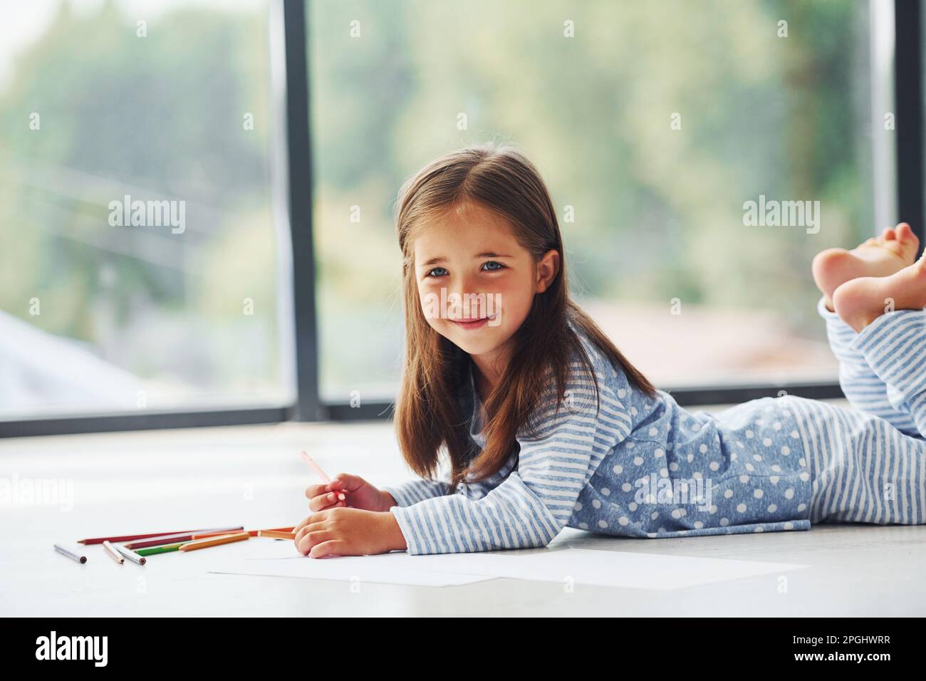 Lying on the floor and drawing. Cute little girl indoors at home alone ...