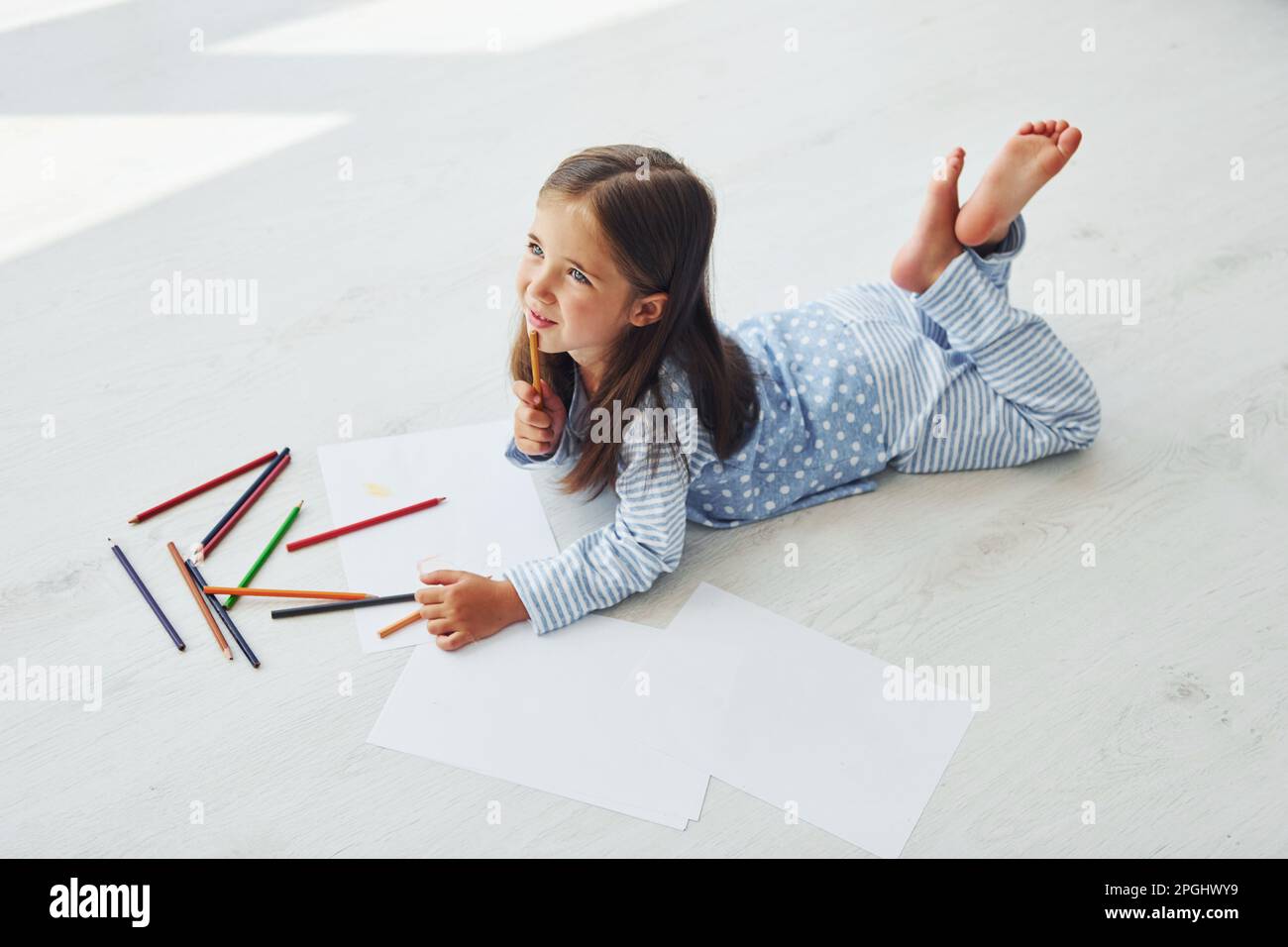 Lying on the floor and drawing. Cute little girl indoors at home alone ...