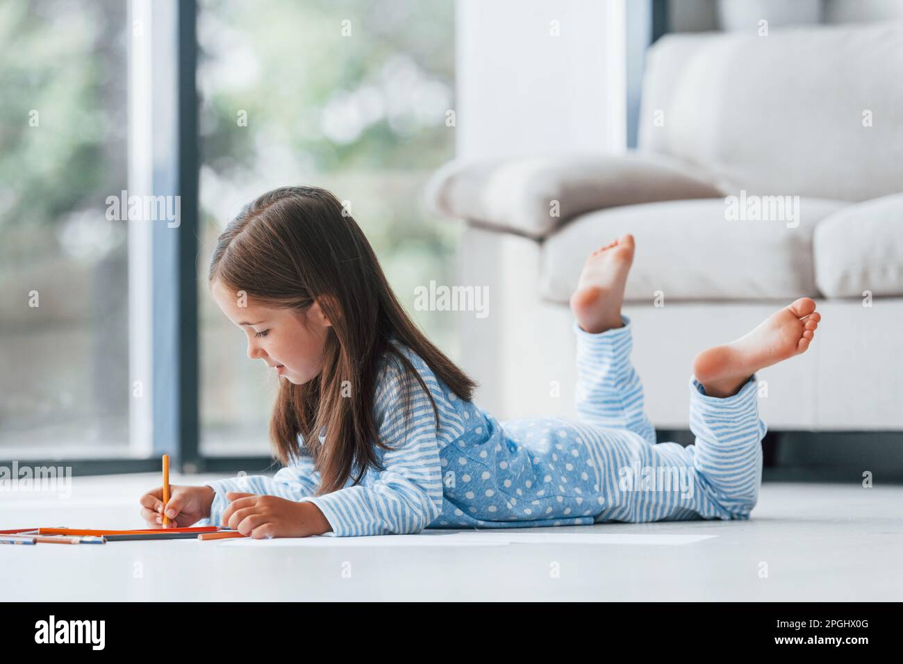 Lying on the floor and drawing. Cute little girl indoors at home alone ...