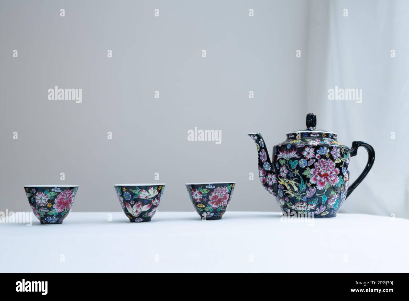 A Chinese teapot and three matching cups stand in a line on a white surface against a pale background suitable for text. Stock Photo