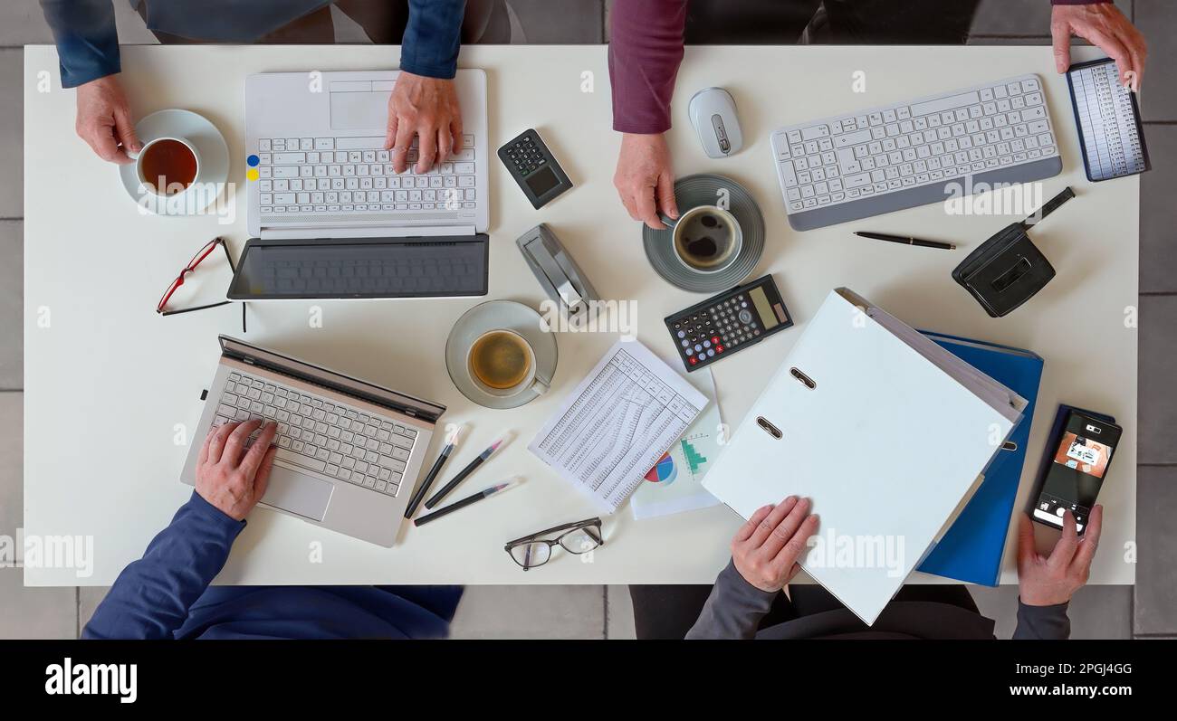 Office desk with hands of for people working together on a joint business project with laptops, papers, calculator and coffee, top view from above, se Stock Photo