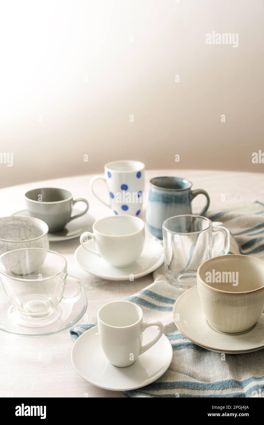Several different empty coffee and tea cups on a round table with a light blue kitchen towel against a beige wall with copy space, selected focus, nar Stock Photo