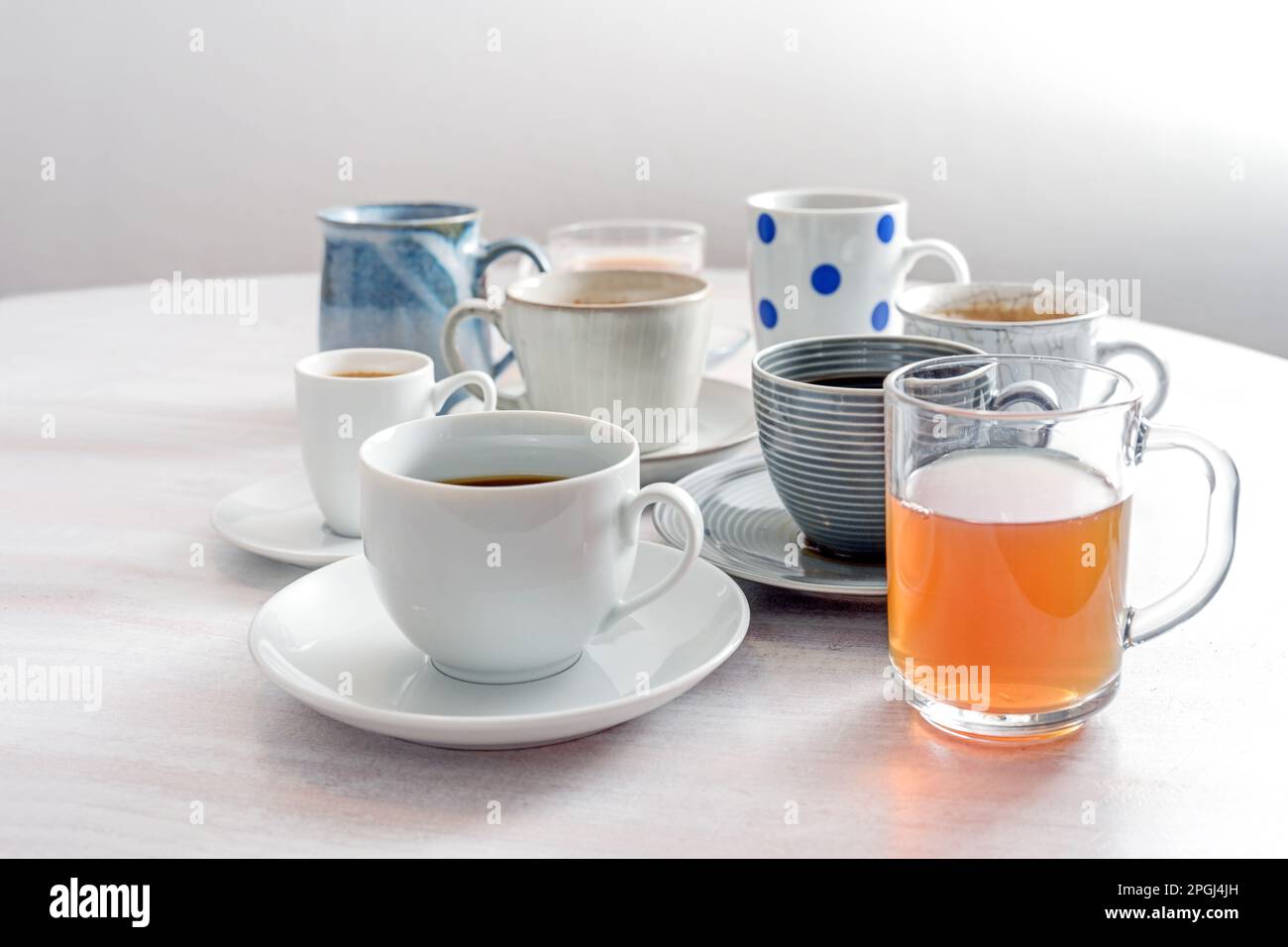 Tea and coffee cups in different styles on a white wooden table against a light gray wall, copy space, selected focus, narrow depth of field Stock Photo