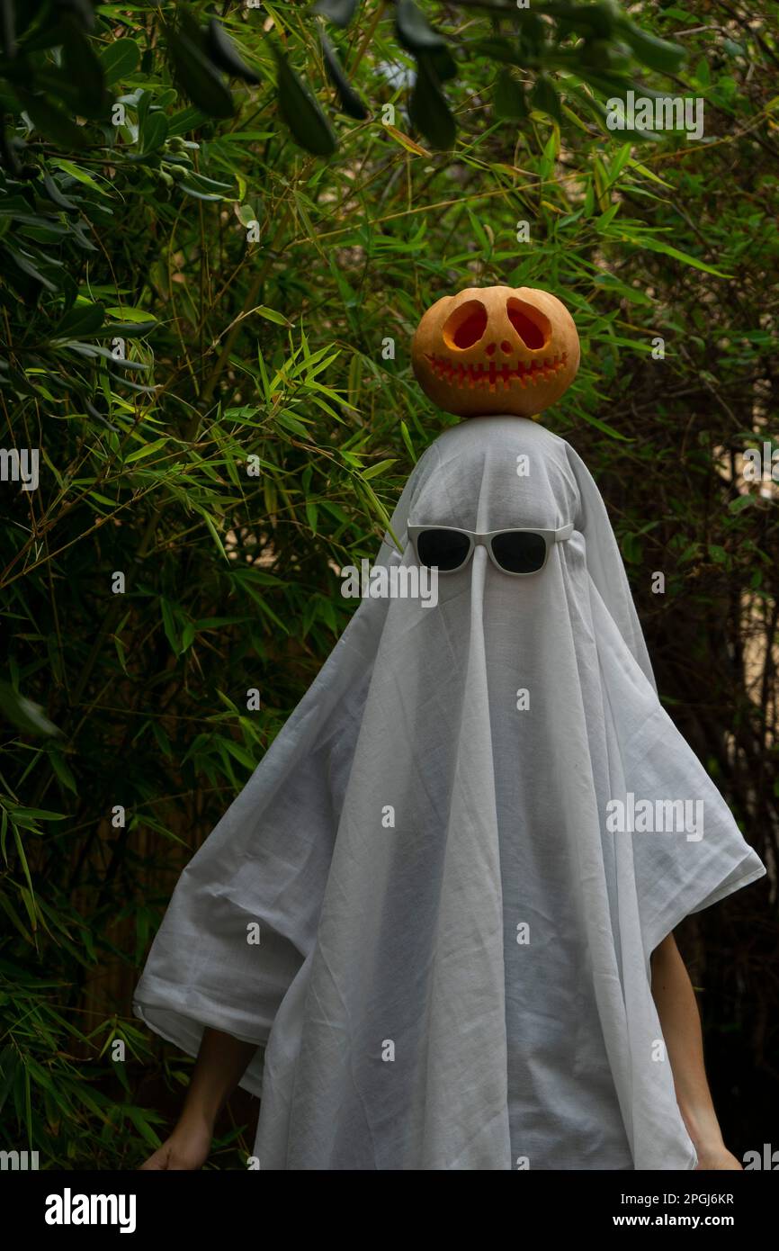 A man dressed in a white ghost costume with sunglasses and a carved pumpkin  atop his head for Halloween Stock Photo - Alamy