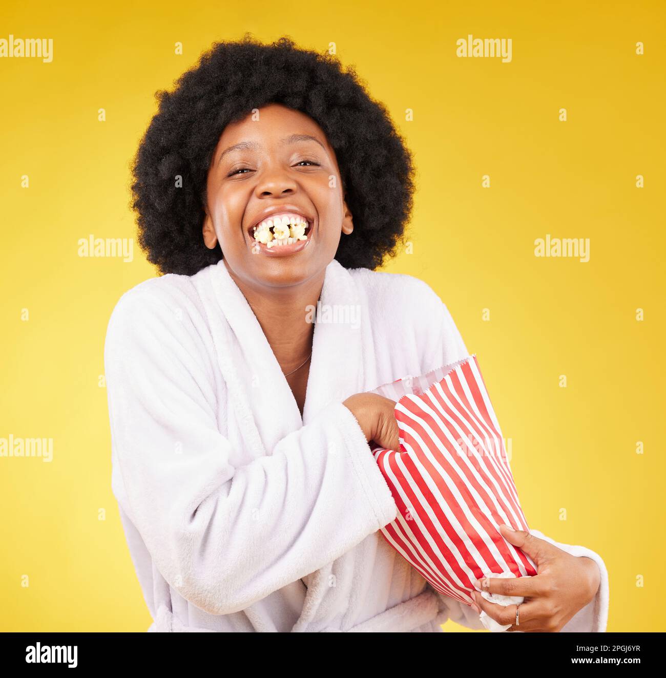 Funny face, portrait and black woman eating popcorn in studio isolated on a yellow background. Comic smile, food and laughing, hungry and happy female Stock Photo
