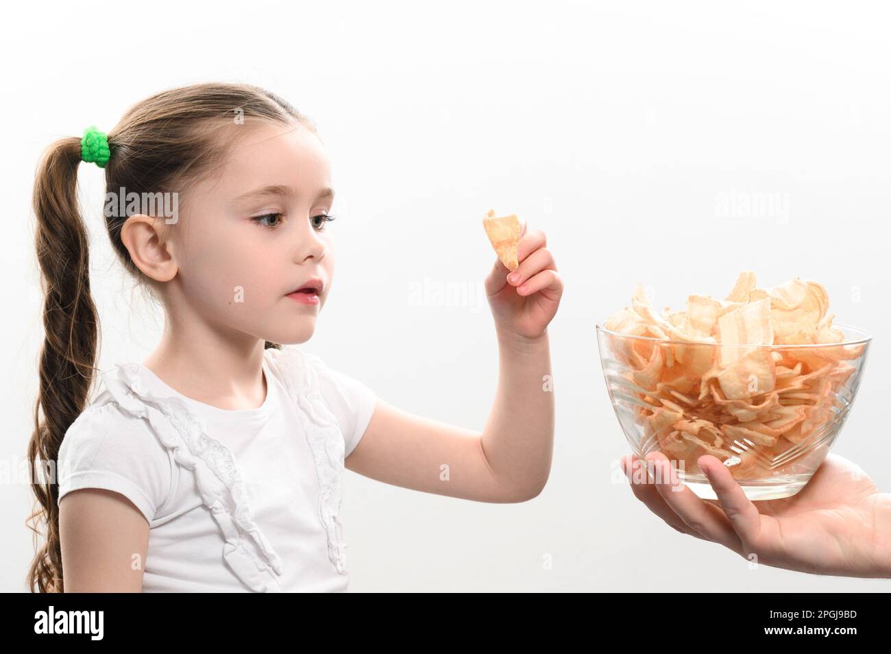 Little girl is given a big bowl of chips snacks with lard, white background portrait of a little
