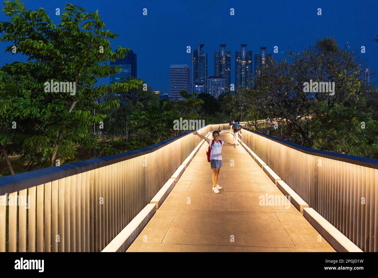 Woman standing on the illuminated walking bridge in Benchakitti park in Bangkok Stock Photo