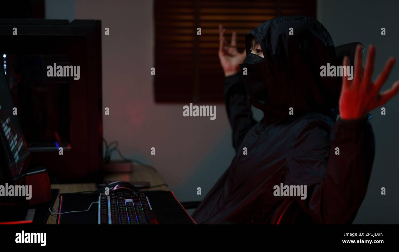 Hacker in hoodie raising hands while having problem with hacking programming system or server. Stock Photo
