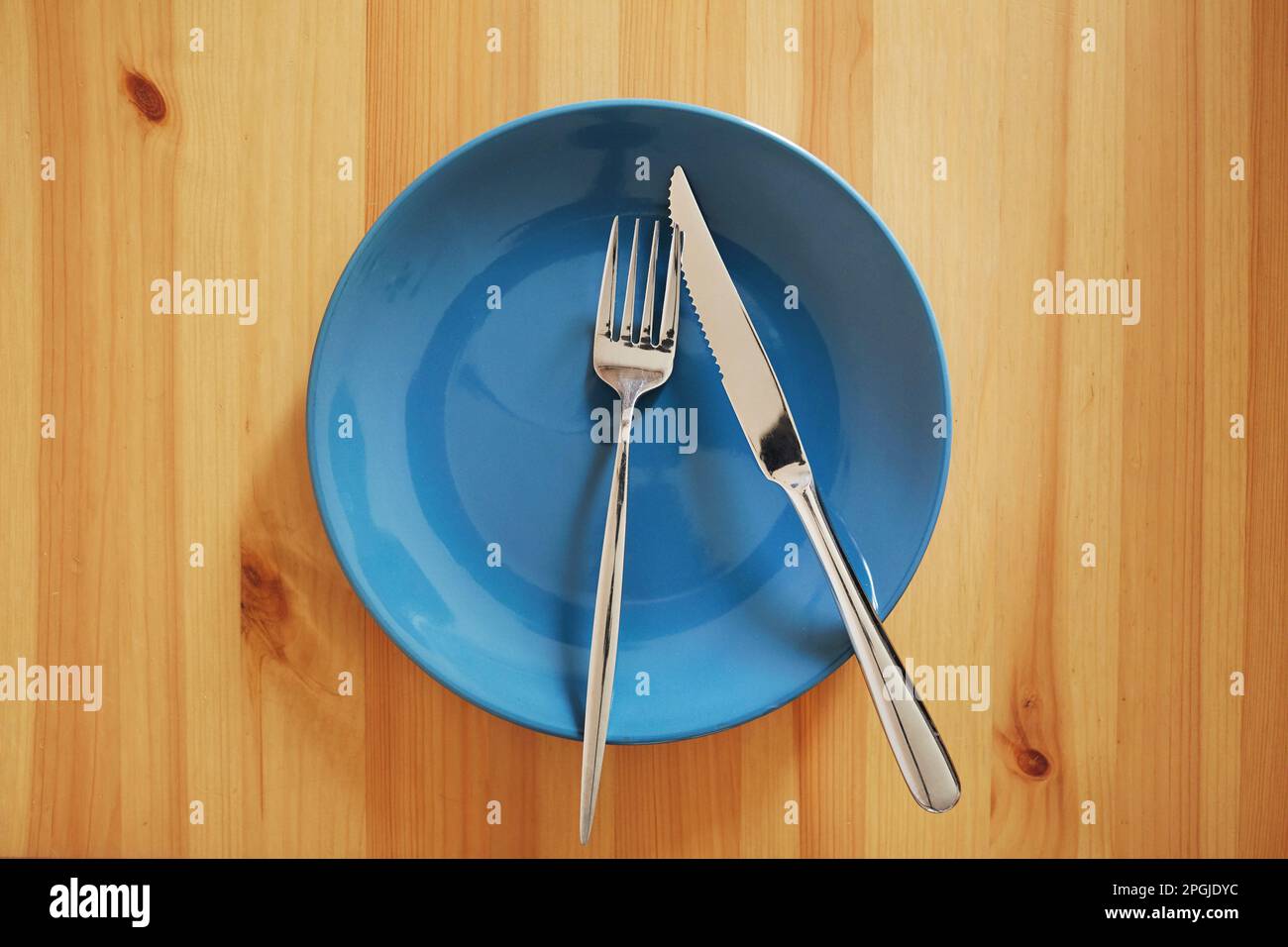 Empty and clean blue plate with fork and knife on a wooden table Stock Photo
