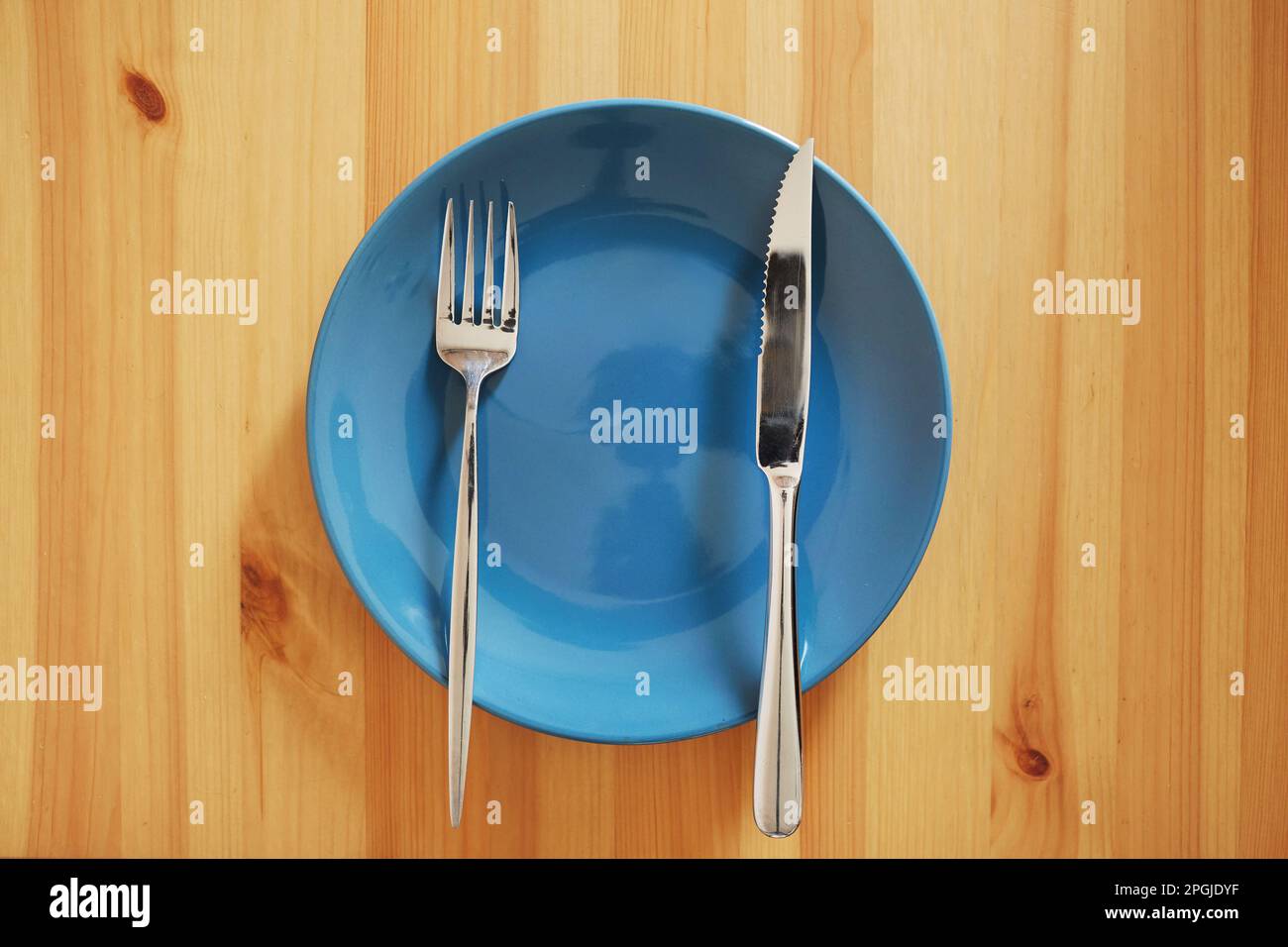 Empty and clean blue plate with fork and knife on a wooden table Stock Photo