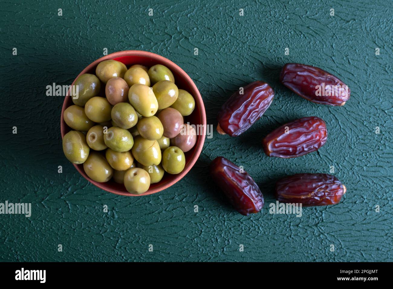 Date fruit with a bowl of green olive on a green background. Stock Photo