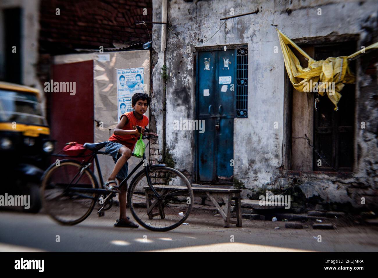 VARANASI, INDIA - OCTOBER 29, 2013: Indian boy stands next to traditional bicycle part in corner of street. Stock Photo
