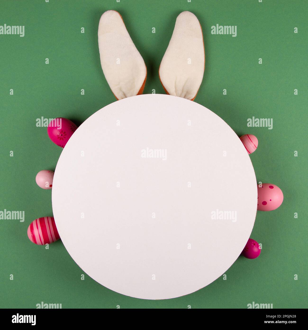 Bunny ears, white circle and Easter eggs on green background Stock Photo