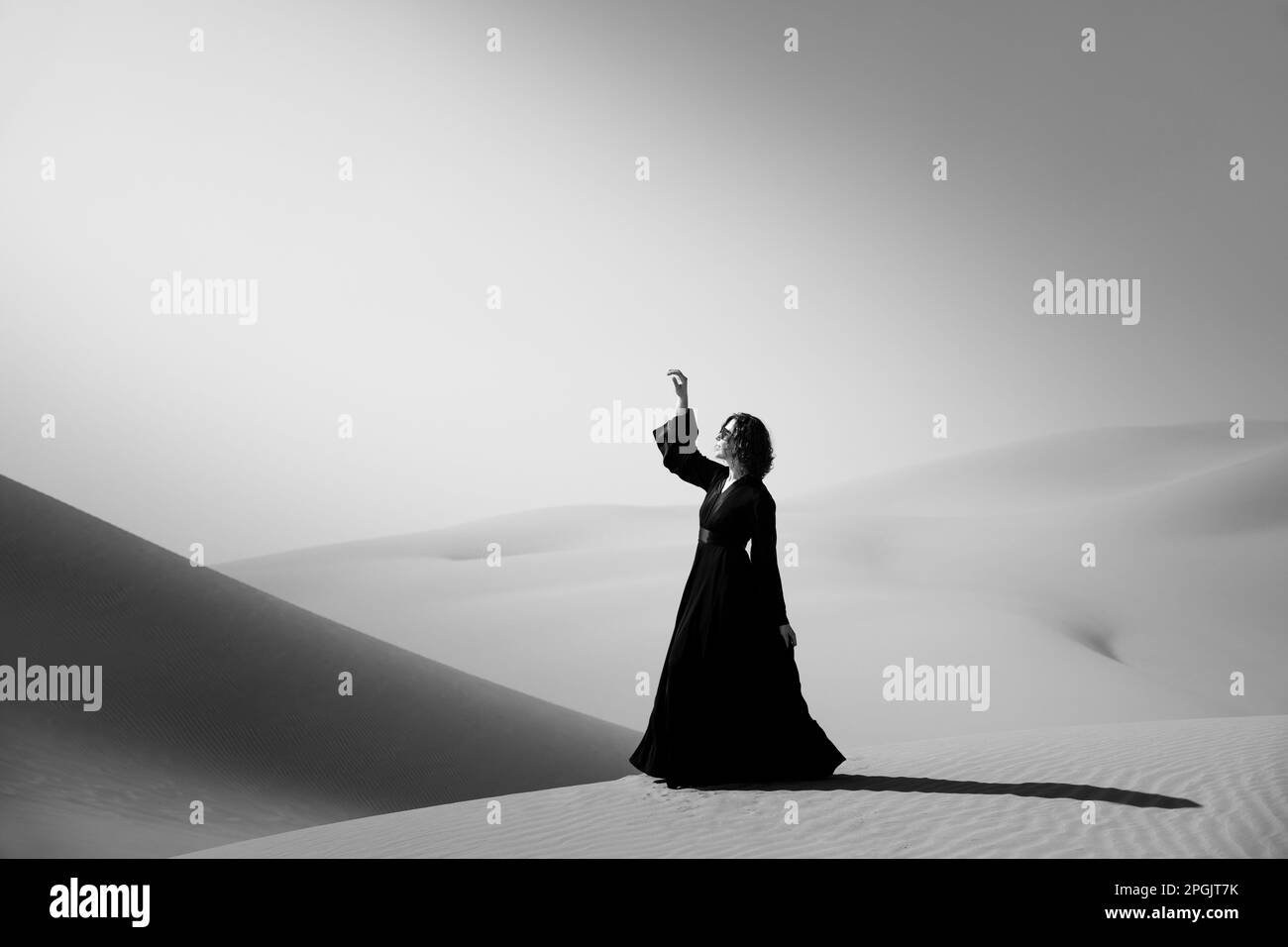 Beautiful young woman with a black abaya walking on the dunes in the desert. Stock Photo