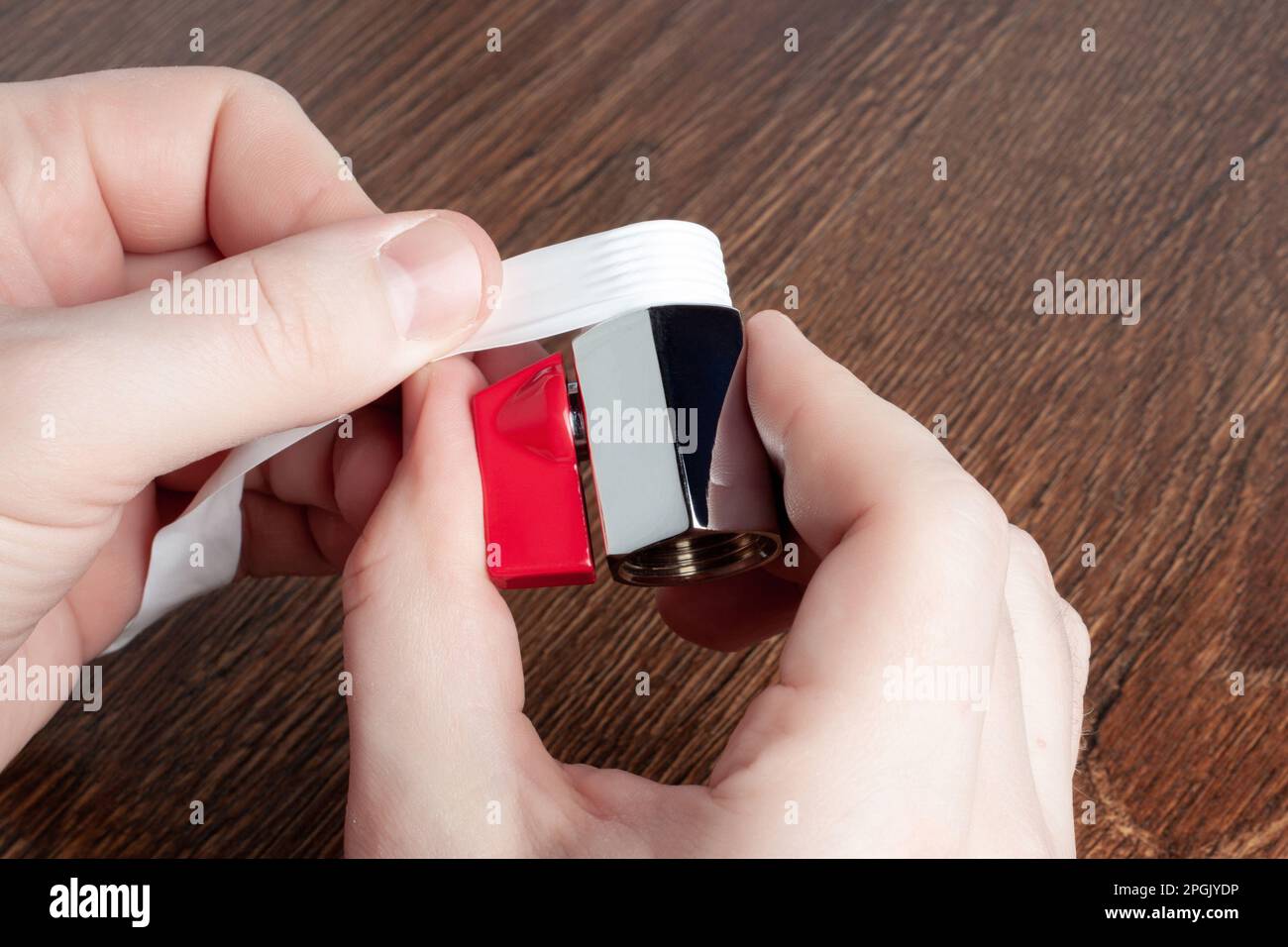 Man using teflon tape to seal water ball faucet with red valve. Wrap