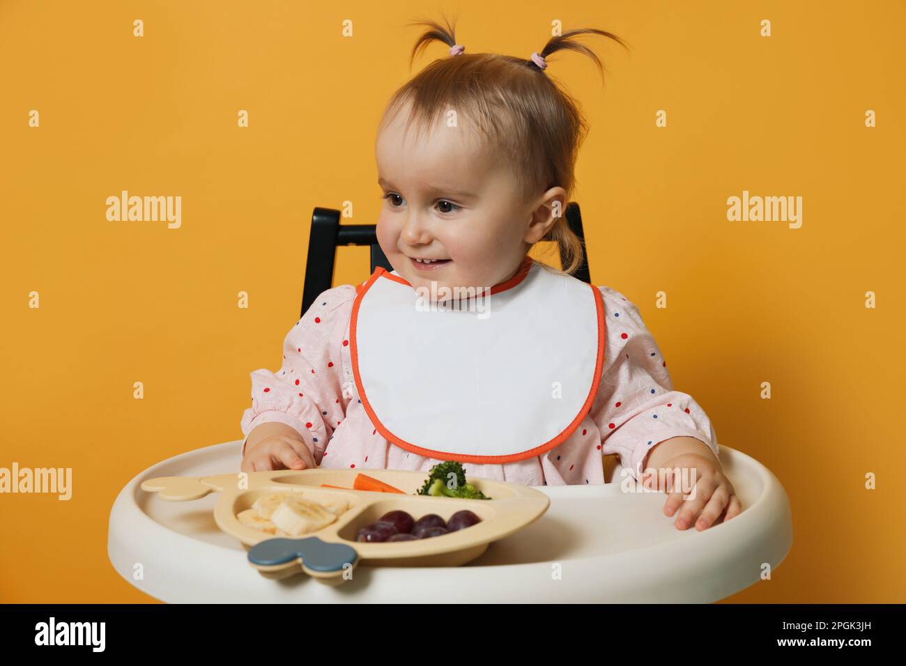 Cute little baby wearing bib while eating on yellow background Stock ...