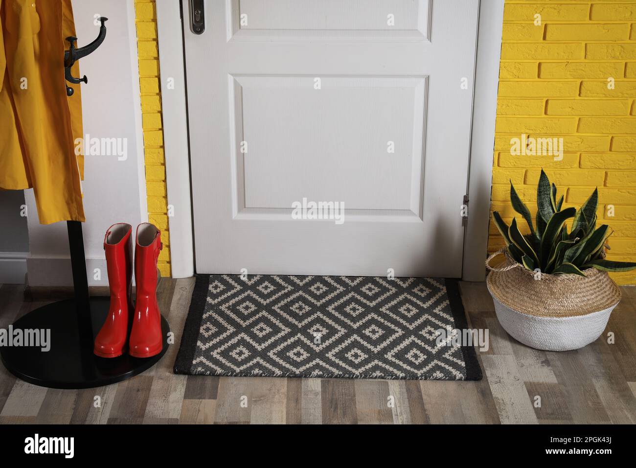 Hallway interior with beautiful houseplant, hanger stand and door mat on floor near entrance Stock Photo