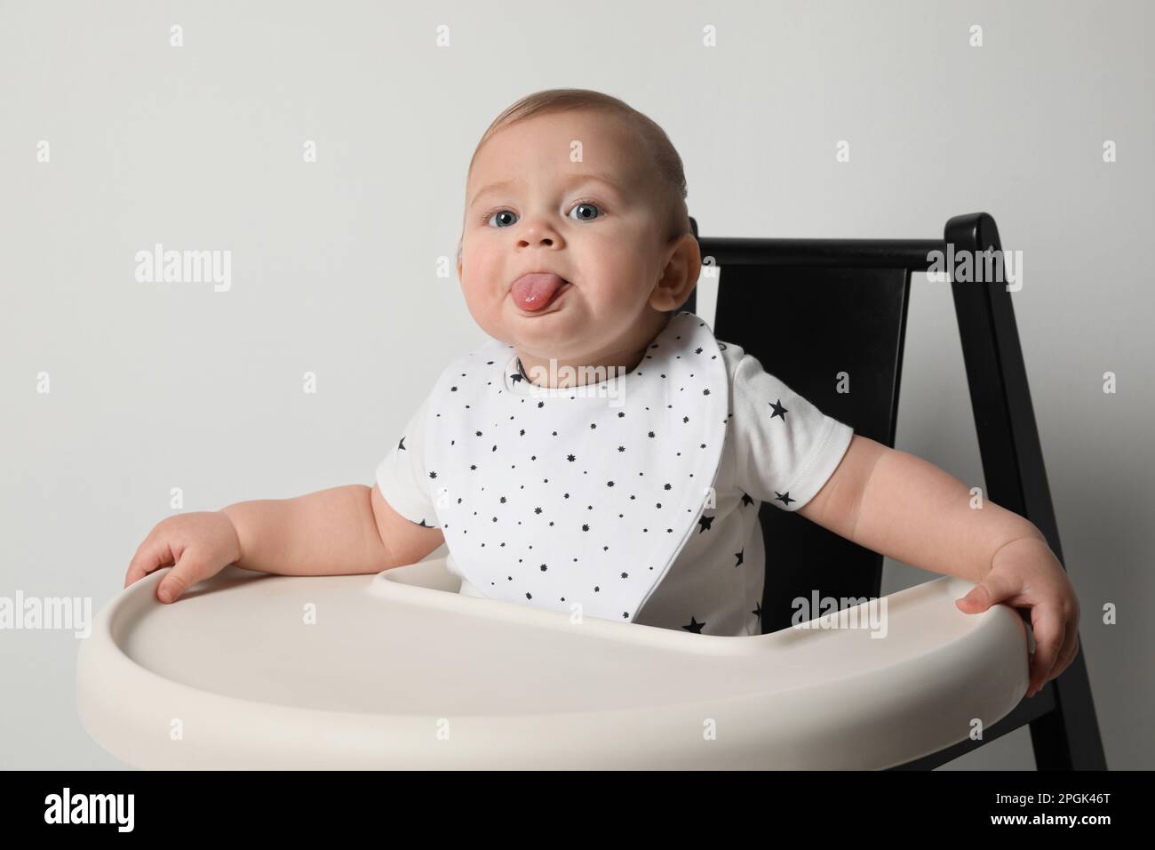 Cute little baby wearing bib in highchair on white background Stock