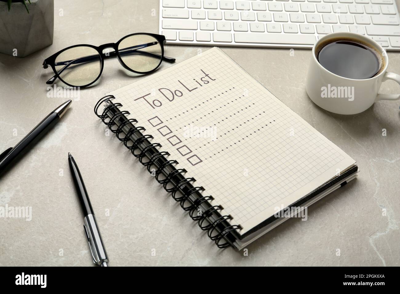 Notepad with unfilled To Do list, pens, glasses and cup of coffee light on grey marble table Stock Photo